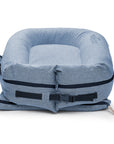 A blue, inflatable travel pillow designed in a U-shape with a zipper and a black adjustable strap. This DockATot Deluxe+ Dock - Indigo Chambray is compact and set against a white background.