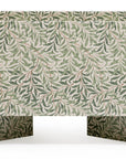 A foldable fabric storage box with a green and white Kind Essential Bassinet - Willow Boughs pattern, designed with two handle cutouts and a structured, boxy shape, featuring ornately crafted pedestal feet, isolated on a