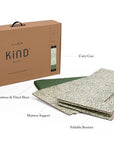 A product image of a foldable Kind Essential Bassinet - Willow Boughs by DockATot that includes a Sorona foam core mattress support and a fitted sheet, all placed next to its packaging box labeled "eco kind bass".